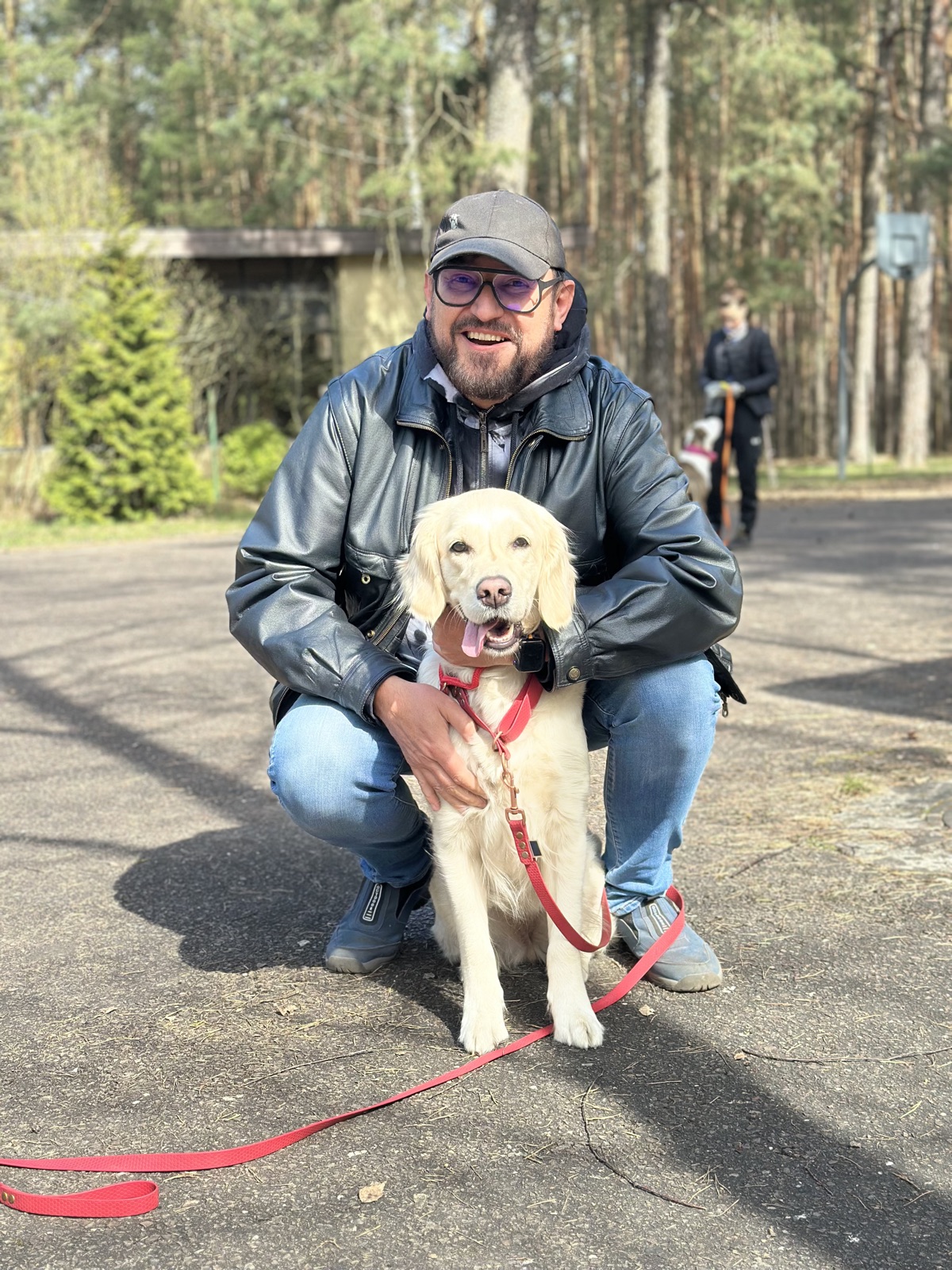 Jacek Gałuszka kuca obok golden retrievera na smyczy